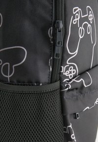 Schwarzer Rucksack mit einem gemusterten Design von weißen Gaming-Controllern, ausgestattet mit einem strukturierten Stoff, einem Netzfach und einem strapazierfähigen Reißverschluss.