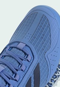 Blue athletic shoe featuring a textured mesh upper, padded tongue, flat laces, and a patterned sole. Accents include dark blue stripes.
