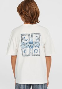 Witte katoenen t-shirt met een grafisch ontwerp op de achterkant in het blauw, met zon- en maamotieven omlijst door intricate patronen.