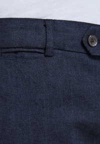 Námořnické modré kalhoty s vzorem herringbone, mají široký pas a jedno knoflíkové zapínání. Texturovaná tkanina se svislými pruhy.