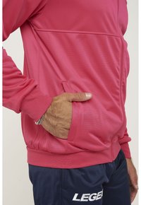 Fitted, texturerad rosa jacka med dragkedja, sidfickor och ribbade ärmmuddar, ihop med marinblå byxor med vit text på låret.