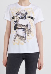 Vit bomulls t-shirt med en svartvit grafik av en staty prydd med blommor, tillsammans med texten "JUST CAVALLI" och ett ljusgult leopardmönster.