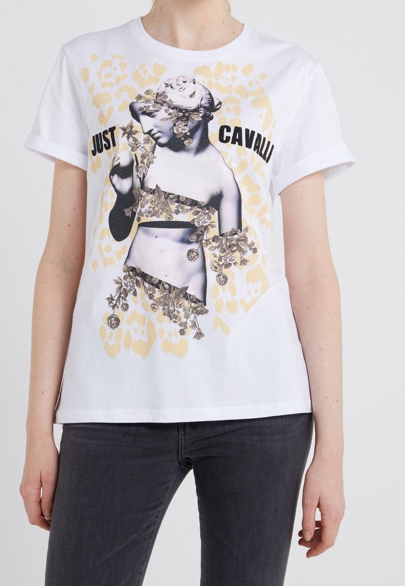 Vit bomulls t-shirt med en svartvit grafik av en staty prydd med blommor, tillsammans med texten "JUST CAVALLI" och ett ljusgult leopardmönster.