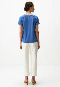 Niebieska koszulka z krótkim rękawem z okrągłym dekoltem, zestawiona z białymi spodniami o szerokich nogawkach. Gładka faktura materiału i luźny krój.