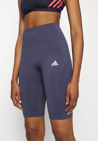 Granatowe rowerowe szorty z wysokim stanem, wykonane z elastycznego, teksturowanego materiału. Na lewej udzie znajduje się biały logo Adidas.