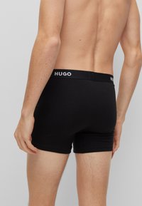 Zwarte boxershorts van een gladde stof met een witte "HUGO" logo op de elastische tailleband. Eenvoudig, aansluitend ontwerp zonder extra patronen.