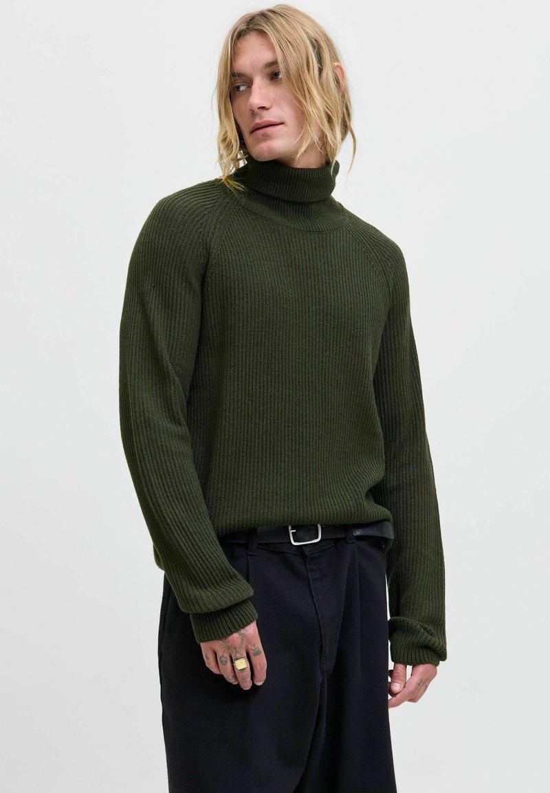 Dunkelgrüner, gerippter Rollkragenpullover mit langen Ärmeln. Er hat eine strukturierte Oberfläche und wird mit schwarzen Hosen kombiniert.