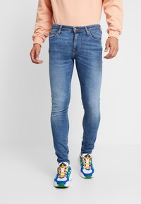 Tunna blå jeans med en blekt finish, femficksdesign och ett kontrasterande midjeband. Matchade med färgglada sportskor.