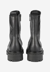 Bottines en cuir noir à finition lisse, avec des fermetures éclair sur les côtés et des semelles en caoutchouc texturé. Un détail de couture court le long des coutures.