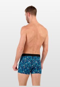 Shorts de boxeur à motifs bleus avec une taille noire ; le design présente des formes géométriques et des motifs abstraits sur un fond vibrant.