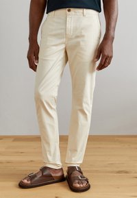 Chinos en coton beige clair avec une coupe ajustée, dot�és d'une fermeture à bouton à l'avant et de poches latérales, associés à des sandales en cuir marron.