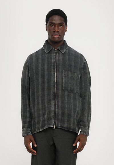 Schwarz- und graues Karo-Zip-Jackett mit einem weit geschnittenen Kragen und einer Brusttasche. Weiche Textur, lässige Passform und kontrastierende Nähte.
