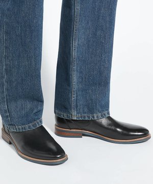 Bottes Chelsea en cuir noir portées avec un jean denim bleu sur un fond clair, montrant les vues latérale et de face des chaussures.
