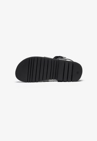 Sort sandal sål med en struktureret overflade, der har dybe riller og forhøjninger til trækkraft. Materialet ser gummilignende og fleksibelt ud.
