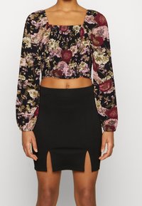 Top corto floreale con maniche lunghe in nero, caratterizzato da fiori rosa e bordeaux. Mini gonna nera a vita alta con doppie aperture laterali.