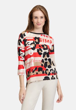Haut à manches longues multicolore avec imprimé léopard, rayures rouges et accents textuels. Fabriqué en tissu doux avec une coupe décontractée et des fentes sur les côtés.
