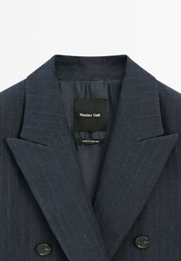 Blazer blu scuro con motivo a righe, design doppiopetto, rever affilati e un'etichetta cucita che reca la scritta "Massimo Dutti" all'interno.