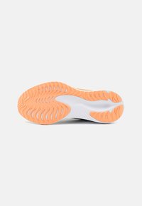 Semelle de chaussure avec une base en caoutchouc blanc texturé et un motif en vagues orange. Présente des rainures pour l'adhérence et la stabilité lors des mouvements.
