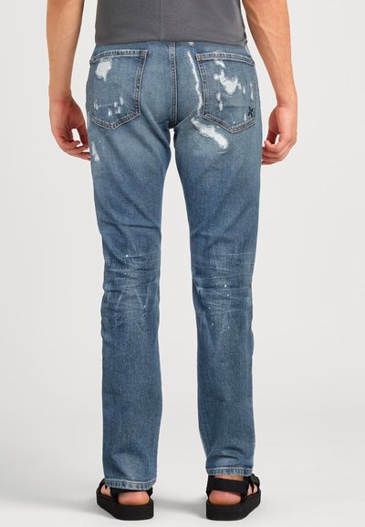 Jeans in denim azzurro chiaro con dettagli strappati, sbiadimenti visibili e macchie di vernice, caratterizzati da una vestibilità standard e cinque tasche.