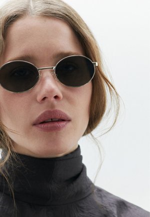 Runde, mørke glas solbriller med metallisk rammedetaljer, sat mod en let tekstureret stofkrave i mørk farve.