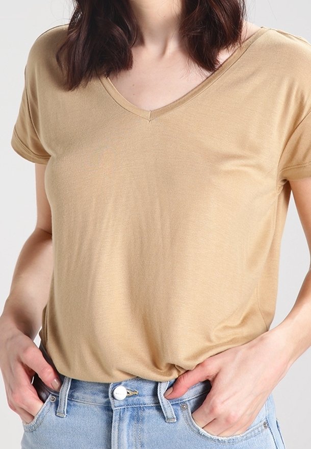 T-shirt beige a V con maniche corte, realizzato in tessuto morbido e leggero. Abbinato a jeans in denim blu a vita alta.