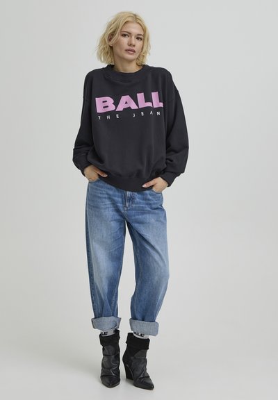 Sweat-shirt noir surdimensionné avec texte graphique rose, associé à un jean denim bleu clair retroussé et des bottines noires ajustées.