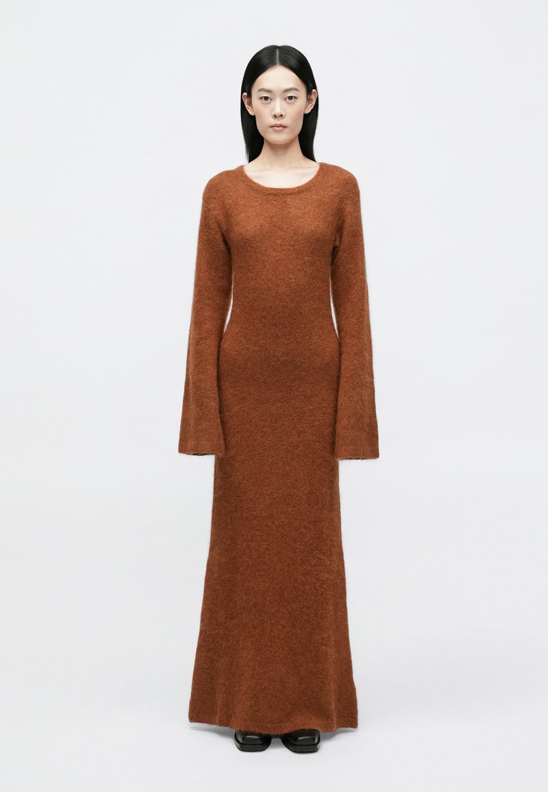 Dolga rjava obleka iz puhastega materiala, z okroglim izrezom in razširjenimi dolgimi rokavi, ima oprijet silhueto in ravno rob.