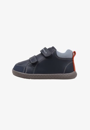 Zapatos de cuero azul marino con tiras de velcro, detalles en gris y una pestaña roja en el talón. Cuenta con una suela de goma flexible con pequeñas perforaciones.