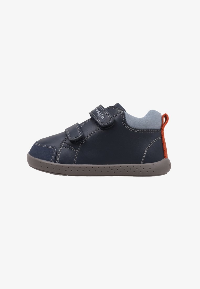 Zapatos de cuero azul marino con tiras de velcro, detalles en gris y una pestaña roja en el talón. Cuenta con una suela de goma flexible con pequeñas perforaciones.