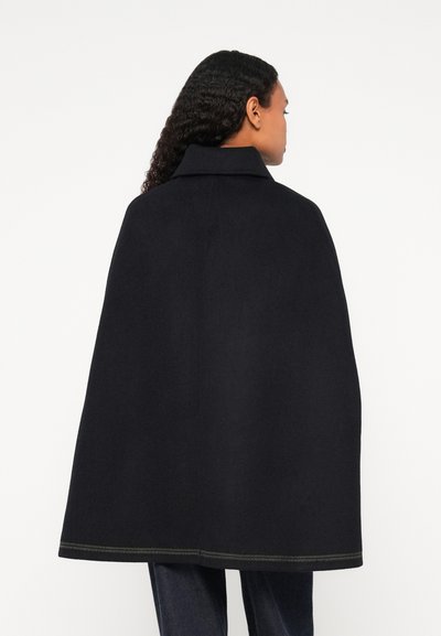 Μαύρος μαλλίνος μανδύας με ψηλό γιακά, με ευδιάκριτη πράσινη ραφή κατά μήκος του στριφώματος, που αναδεικνύει μια ρο streamlined σιλουέτα και υφασμάτινη υφή.