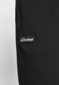 Svarta träningsoveraller tillverkade av mjukt tyg, med en vertikal söm och en rektangulär ellesse-logotyp på vänster sida.