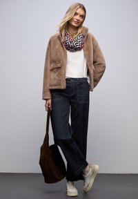 Veste en fausse fourrure beige, haut blanc, jeans larges en denim foncé, écharpe à motifs noir et rose, sac fourre-tout marron, baskets blanches.