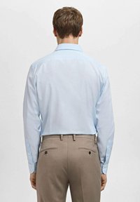Jasnoniebieska koszula z długim rękawem z ostrym kołnierzykiem, mankietami na guziki i gładką fakturą. W połączeniu z beżowymi spodniami z dwoma tylnymi kieszeniami.