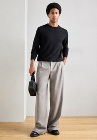 Pulover negru, pantaloni gri largi și geantă neagră. Textură netedă, pulover ajustat, pantaloni plisați și pantofi comozi. Design minimalist.