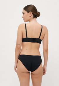 Črn modrček in usklajeni bikini spodnji del, ki vključujeta gladko teksturo, nastavljive naramnice in zaponko zadaj. Minimalističen dizajn.