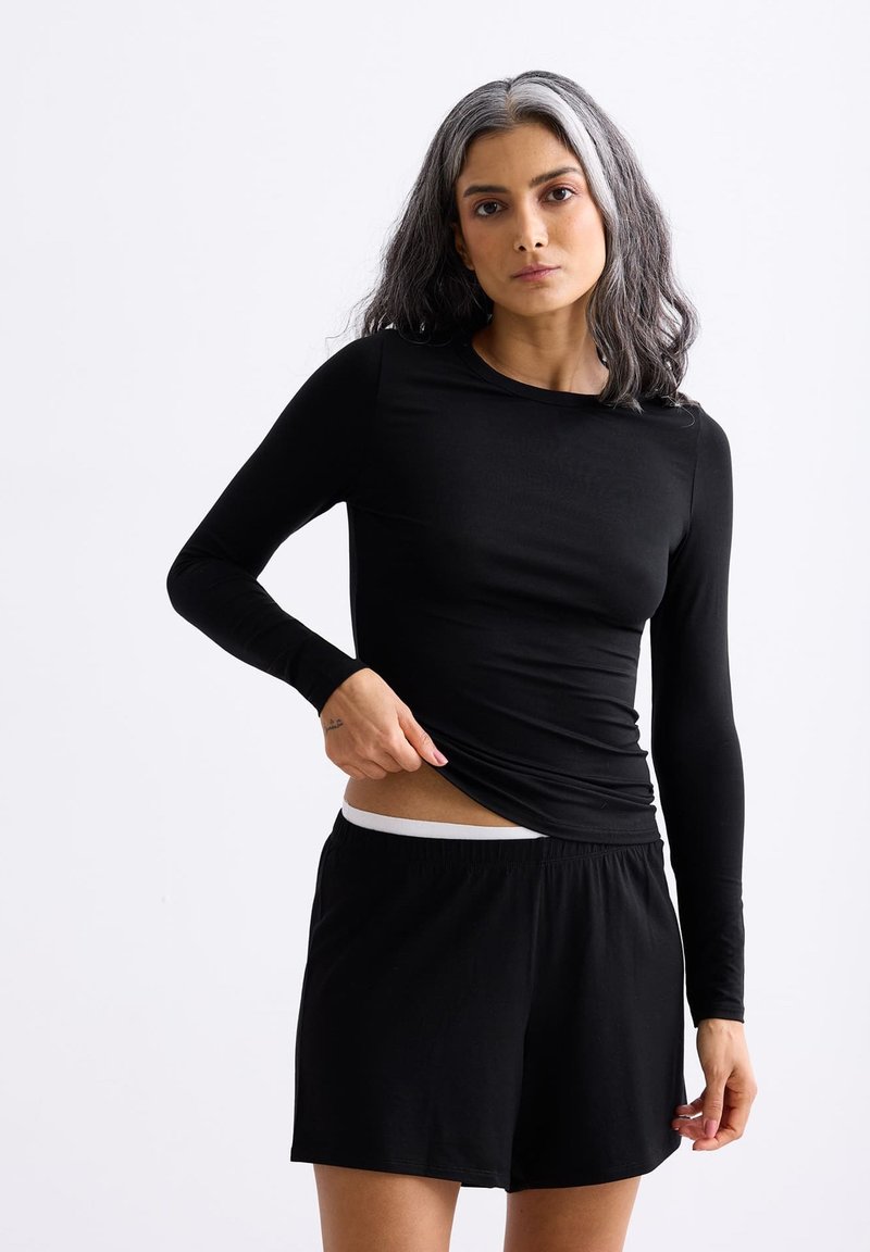 Zwarte langcorpus top van een zachte, rekbare stof, gecombineerd met zwarte shorts met een witte tailleband. Eenvoudig, strakke ontwerp zonder patronen.