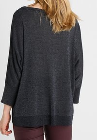 Czarny sweter z połyskiem o luźnym kroju, z rękawami typu nietoperz i prążkowanym dołem. Wykonany z miękkiego, teksturowanego materiału, odpowiedni do noszenia warstwowego.