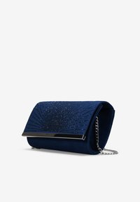 Bolso de mano de ante azul marino con herrajes plateados y un patrón de adornos brillantes en el frente. Cuenta con una correa de cadena para llevarlo.