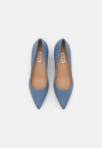 Chaussures en cuir bleu à bout pointu avec une texture lisse, un design minimaliste et une semelle intérieure beige portant le logo "GUESS".