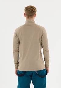 Lichtbeige langemouw overhemd met een hoge kraag en een getailleerd ontwerp, gemaakt van soepel stof. Draagt met teal kleurige broek met een riemdetails.