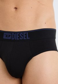 Schwarze Slips mit weicher Textur, ausgestattet mit einem dunkelblauen elastischen Bund mit "DIESEL"-Logo. Figurbetontes, minimalistisches Design.