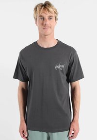 T-shirt en coton gris foncé avec col rond, manches courtes et petit logo blanc sur le côté gauche de la poitrine. Texture douce.