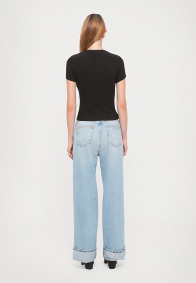 Black short-sleeve top paired with light blue wide-leg jeans featuring rolled cuffs and a relaxed fit, viewed from the back.
