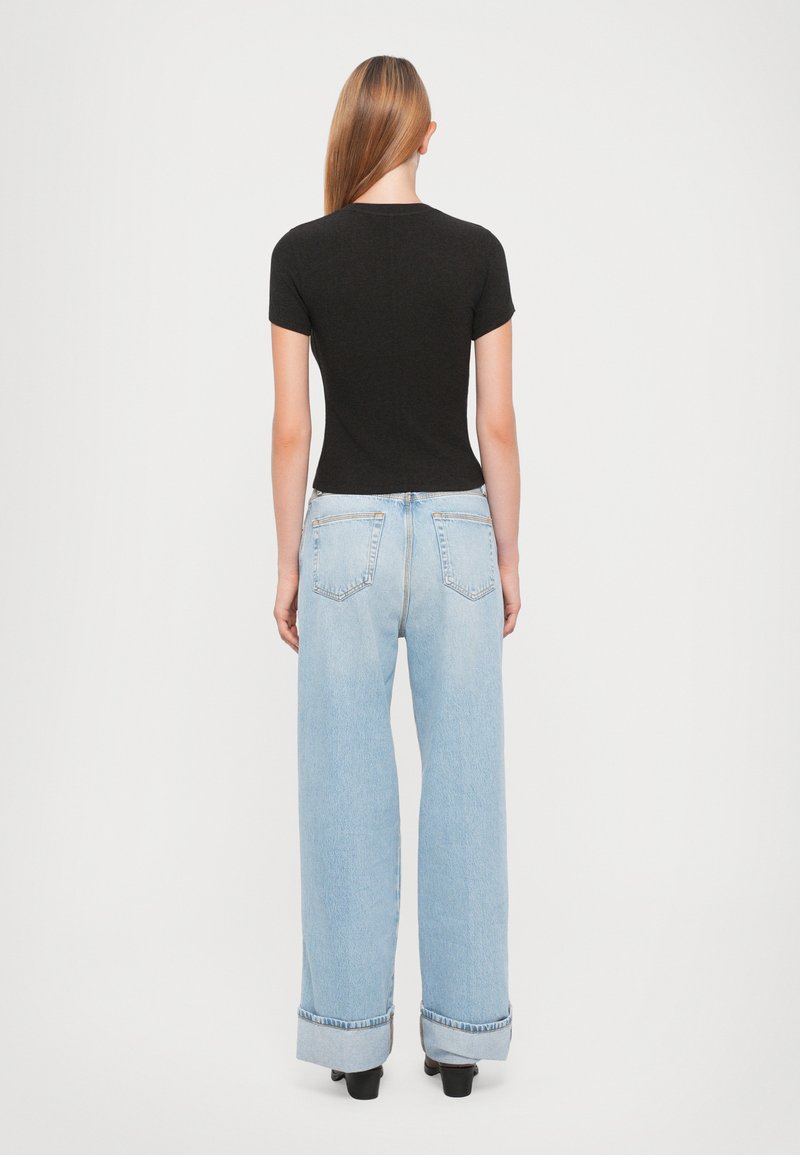 Black short-sleeve top paired with light blue wide-leg jeans featuring rolled cuffs and a relaxed fit, viewed from the back.