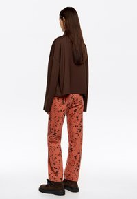 Ruda megzta palaidinė, rusvai raudonos kelnės su juodais purslais, ir tamsūs zomšiniai batai. Lygus paviršius ir laisva iškirptė.