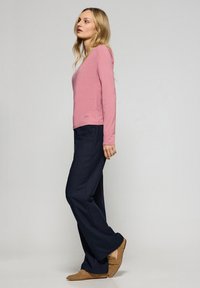 Ljusrosa långärmad topp med V-ringning, ihop med mörkblå byxor och beige skor. Slät tyg; avslappnad passform.