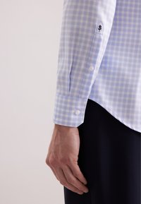 Manica di camicia a quadri azzurri e bianchi con polsino bottonato; presenta un ricamo floreale sul polsino. Texture in cotone liscia.