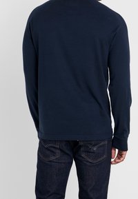 Navyblaues Langarmshirt mit Rundhalsausschnitt, aus weichem Baumwollstoff, mit Raglansleeves und bequemer Passform, kombiniert mit dunklen Jeans.