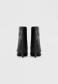 Pair of black leather ankle boots with slim heels, viewed from the back on a plain light gray background.