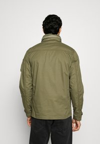 Olivgrön, lätt jacka med en fällbar krage, långa ärmar och sydda detaljer. Enkelt design, passar för avslappnad klädsel.